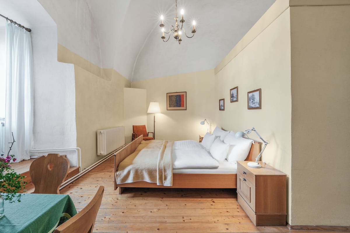 A bedroom with a wooden bed, bedside tables, a lamp, a radiator, and a window with curtains.