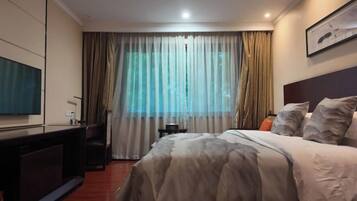 A hotel room with a bed, a desk, a chair, a television, and a window with curtains.