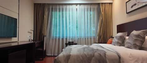 Habitación de hotel con cama, escritorio, silla, televisor y ventana con cortinas.