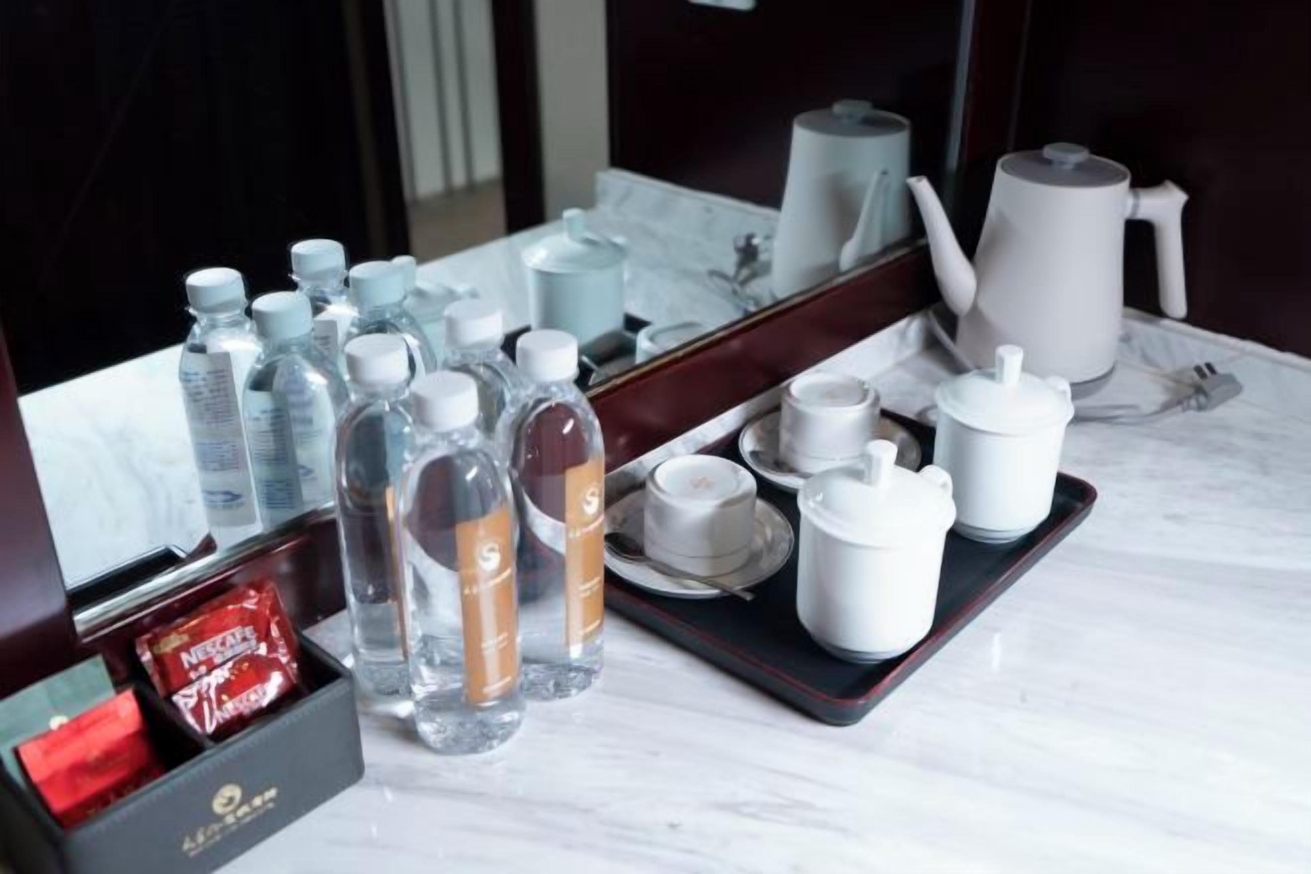 A hotel room's bathroom with a mirror, toiletries, and a tray with cups and a teapot.
