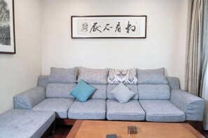 A grey sectional sofa with patterned cushions, a framed artwork above, and a wooden coffee table with a remote control.