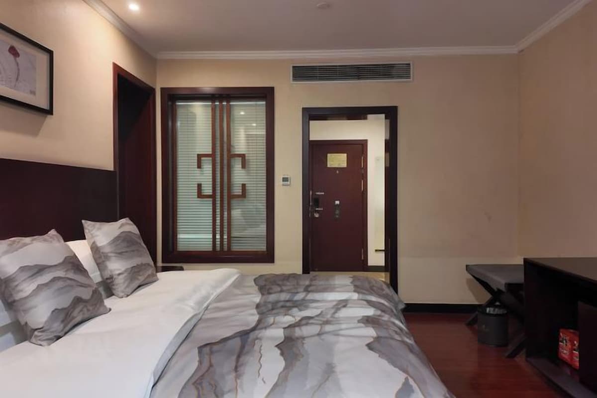 A hotel room with a bed, a desk, a chair, and a door.