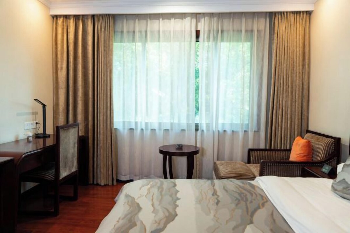 A hotel room with a bed, a desk, a chair, and a window with curtains.