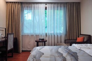 A hotel room with a bed, a chair, a small table, and a window with curtains.