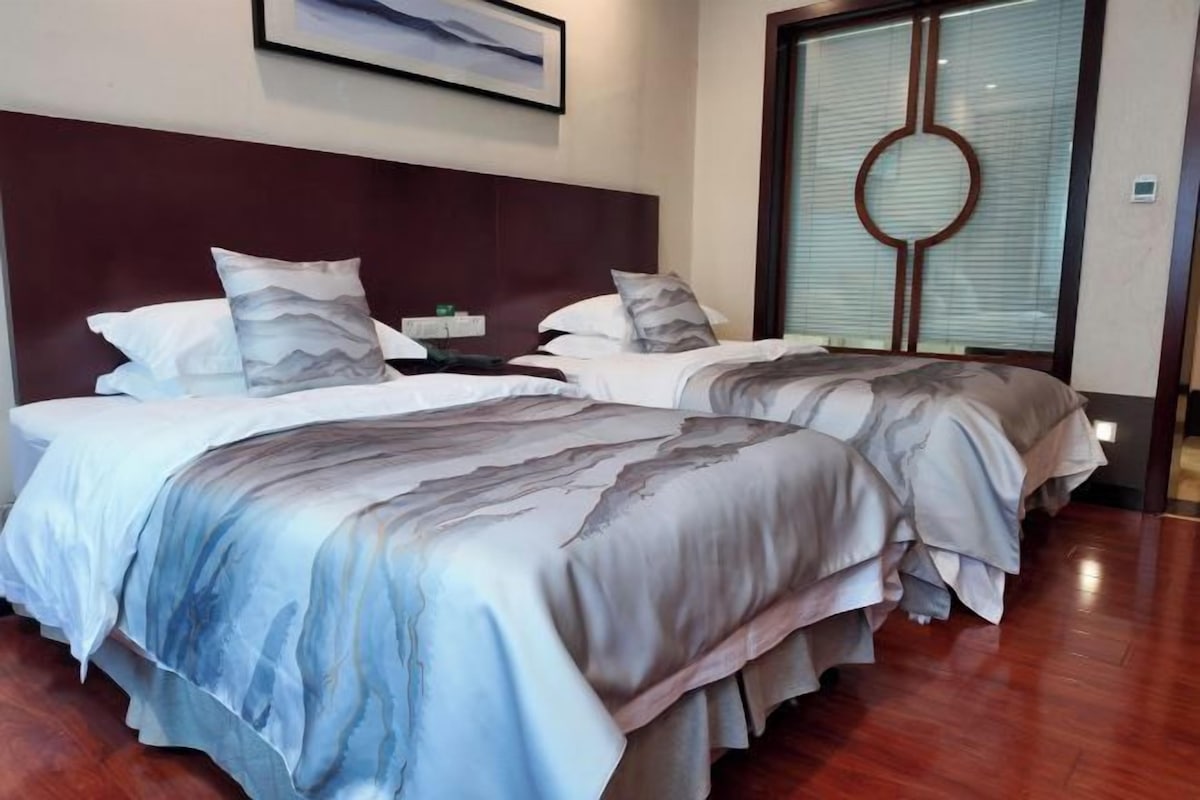 A hotel room with two beds, a wooden floor, and a large window with a decorative frame.