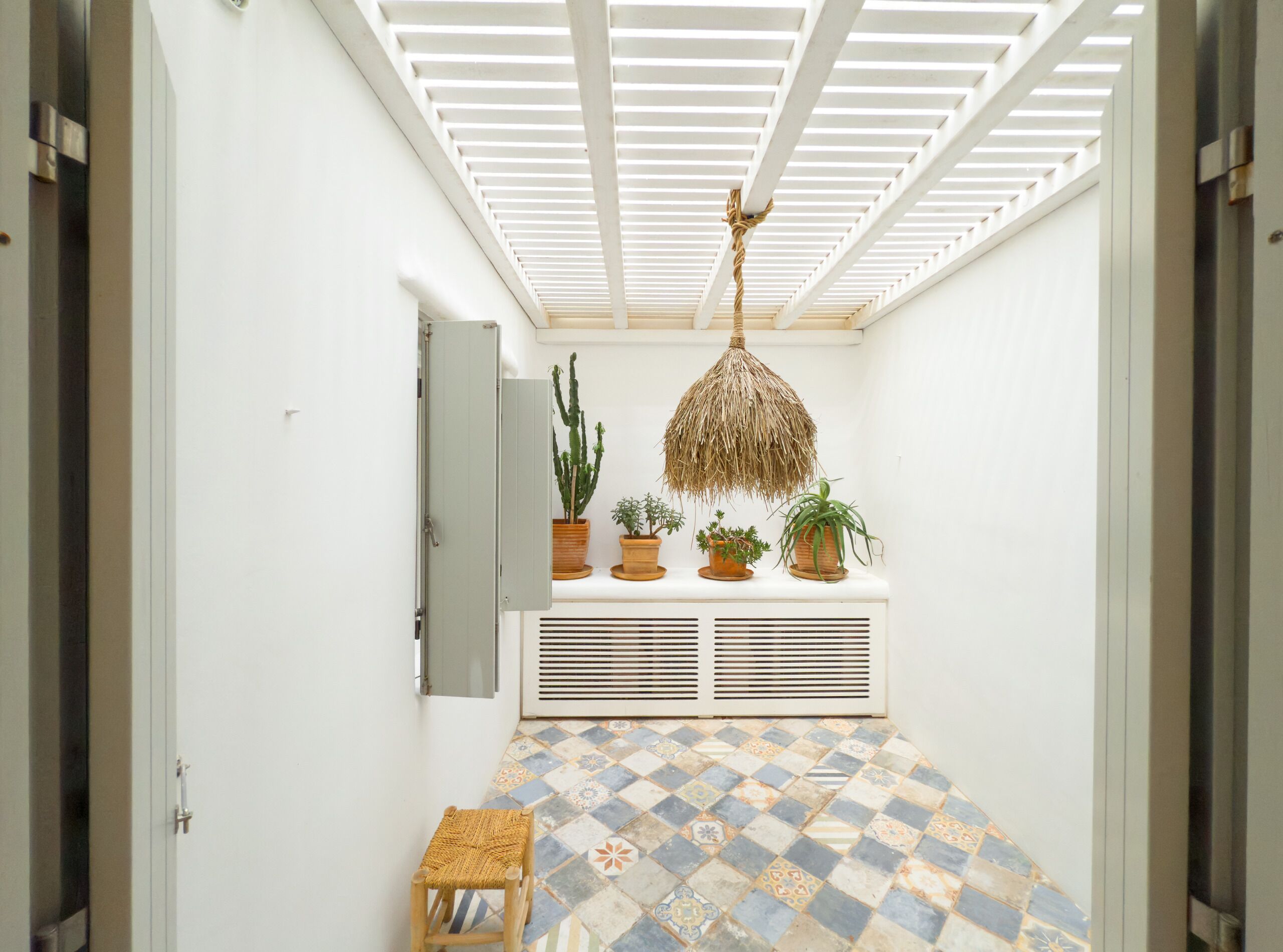 A narrow hallway with a sloped ceiling, a woven ceiling light, a radiator, and a tiled floor.