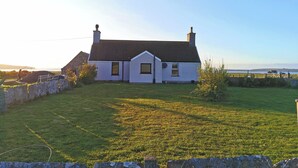 A white house with a sloped roof, a chimney, and a well-maintained lawn. - Cosy Highland retreat with countryside and sea views. (John o' Groats)