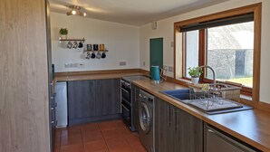 A compact kitchen with a washing machine, a sink, and a window providing a view of the outside. - Cosy Highland retreat with countryside and sea views. (John o' Groats)