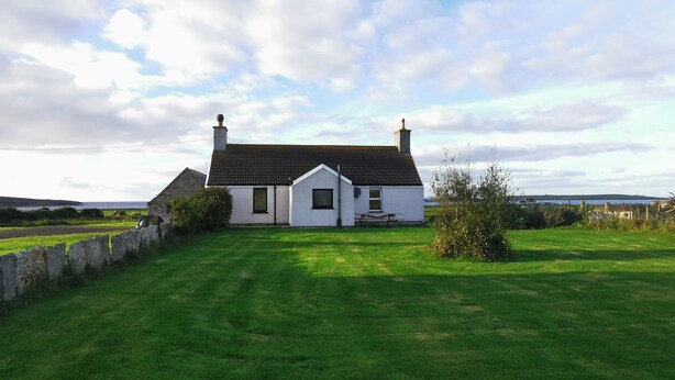 A white house with a black roof, a stone wall, and a grassy lawn. - Cosy Highland retreat with countryside and sea views. (John o' Groats)