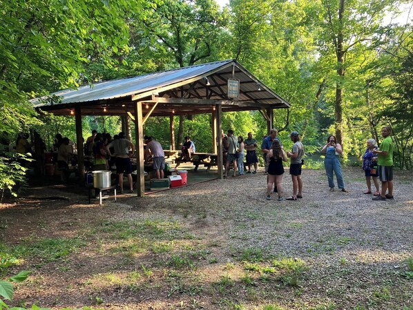 A covered pavilion with picnic tables and a grill area, surrounded by trees.