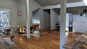 Una habitación amplia con piso de madera, ventilador de techo, kitchenette con refrigerador y microondas, y un banco de madera.