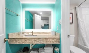 Ein Badezimmer mit einer türkis farbenen Wand, einer Granit-Arbeitsplatte, einem weißen Waschbecken und einer weißen Toilette.
