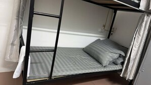 A bunk bed with a mattress and pillows, a curtain, and a wall socket.
