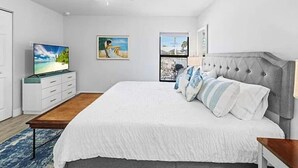 A bedroom with a large bed, a ceiling fan, a TV on a dresser, and artwork on the walls.