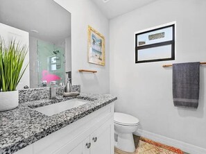 A bathroom with a granite countertop, white cabinets, a white toilet, a framed picture on the wall, and a towel rack. - Tropical Palms On The Serene Canal (Cape Coral)