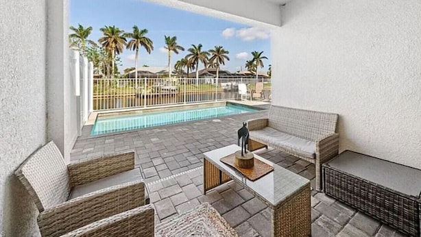A patio area with wicker furniture, a pool, and palm trees in the background.