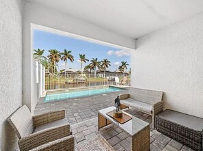 A patio area with wicker furniture, a pool, and palm trees in the background. - Tropical Palms On The Serene Canal (Cape Coral)