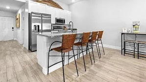 A modern kitchen with a central island, stainless steel appliances, and four wicker chairs.