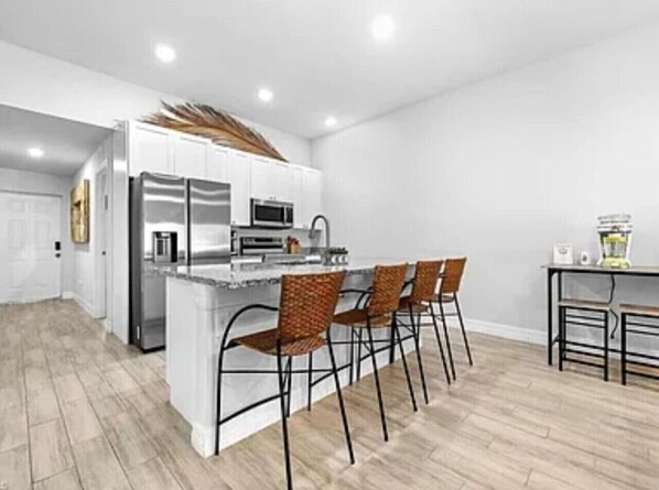 A modern kitchen with a central island, stainless steel appliances, and four wicker chairs. - Tropical Palms On The Serene Canal (Cape Coral)