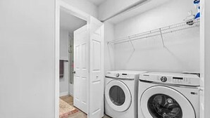 A laundry room with two front-loading washing machines, a drying rack, and a door leading to another room.