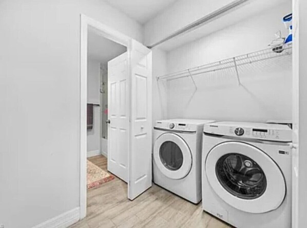 A laundry room with two front-loading washing machines, a drying rack, and a door leading to another room. - Tropical Palms On The Serene Canal (Cape Coral)