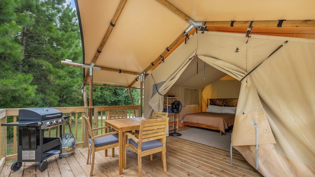 Un hébergement sous tente doté d’une terrasse en bois, d’un barbecue et d’un lit à l’intérieur.