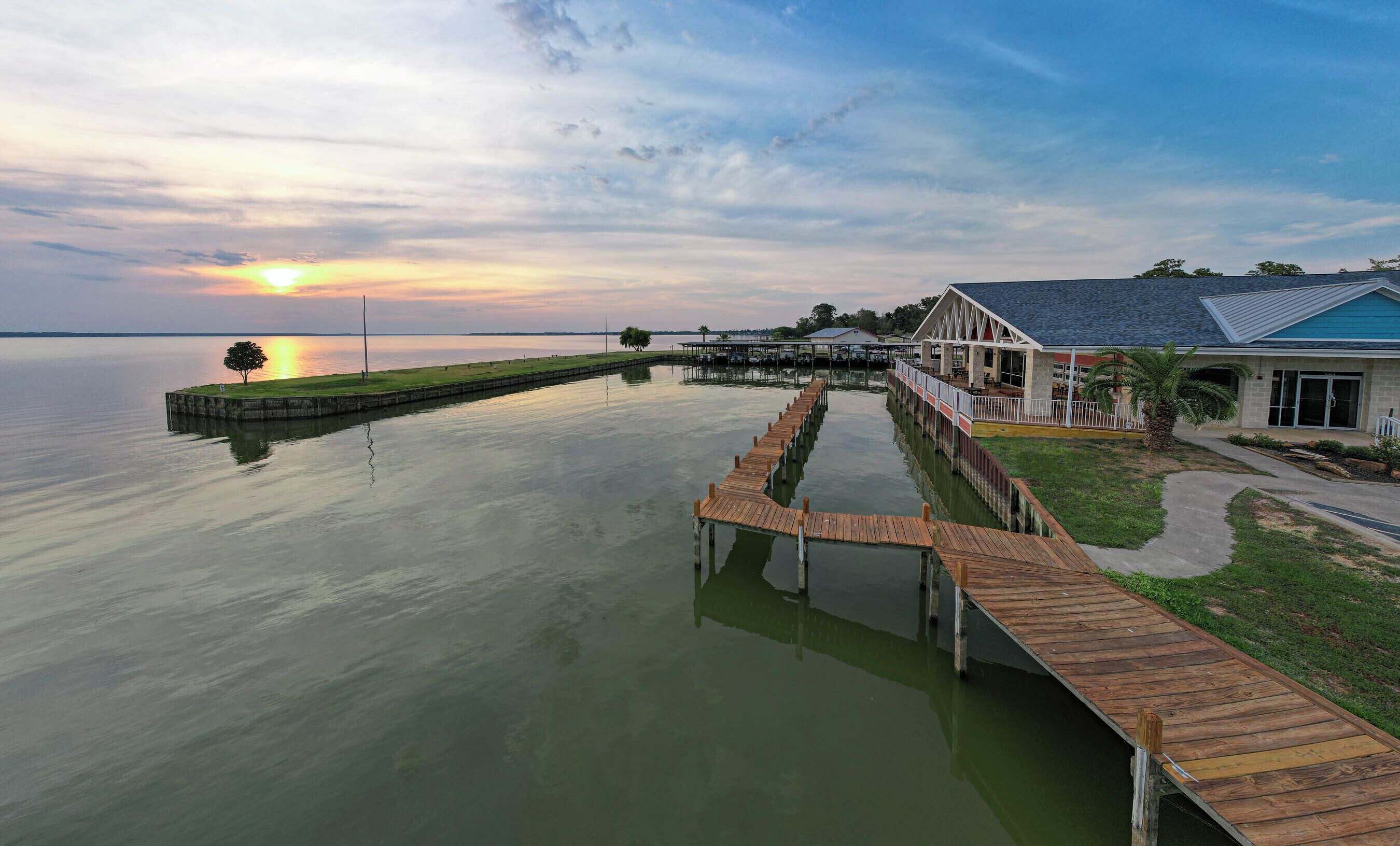 A waterfront property with a wooden dock extending into calm water, a covered outdoor seating area, and a building with a blue roof.