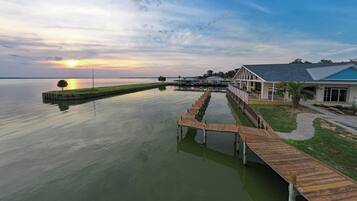 A waterfront property with a wooden dock extending into calm water, a covered outdoor seating area, and a building with a blue roof.