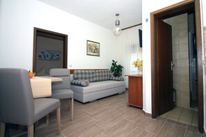 Una sala de estar moderna con un sofá gris, una mesa de comedor con dos sillas, una mesita de madera y una planta en maceta.