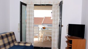 A living room with a sofa, a television on a wooden stand, and a view of an outdoor patio with a table and chairs. - Zadar Coastal Haven - One Bedroom Apartment With Sea View (Zadar)