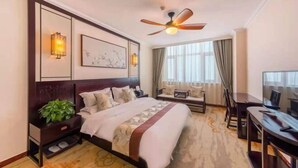 A hotel room with a large bed, a desk, a television, a ceiling fan, and a window with curtains. - New Shilong Hotel (Shijiazhuang)