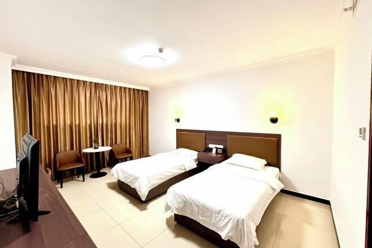 Ein Hotelzimmer mit zwei Einzelbetten, einem Schreibtisch mit Stuhl, einem kleinen Tisch und einem Fernseher.