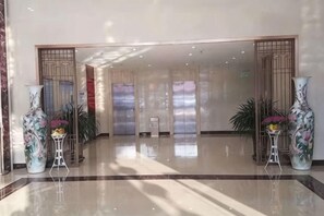 Un hall d’hôtel avec un sol ciré, un comptoir de réception et un grand vase rempli de fleurs.