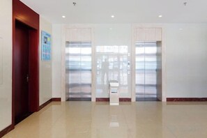 Un couloir avec deux ascenseurs, une porte à gauche et un petit kiosque au centre.