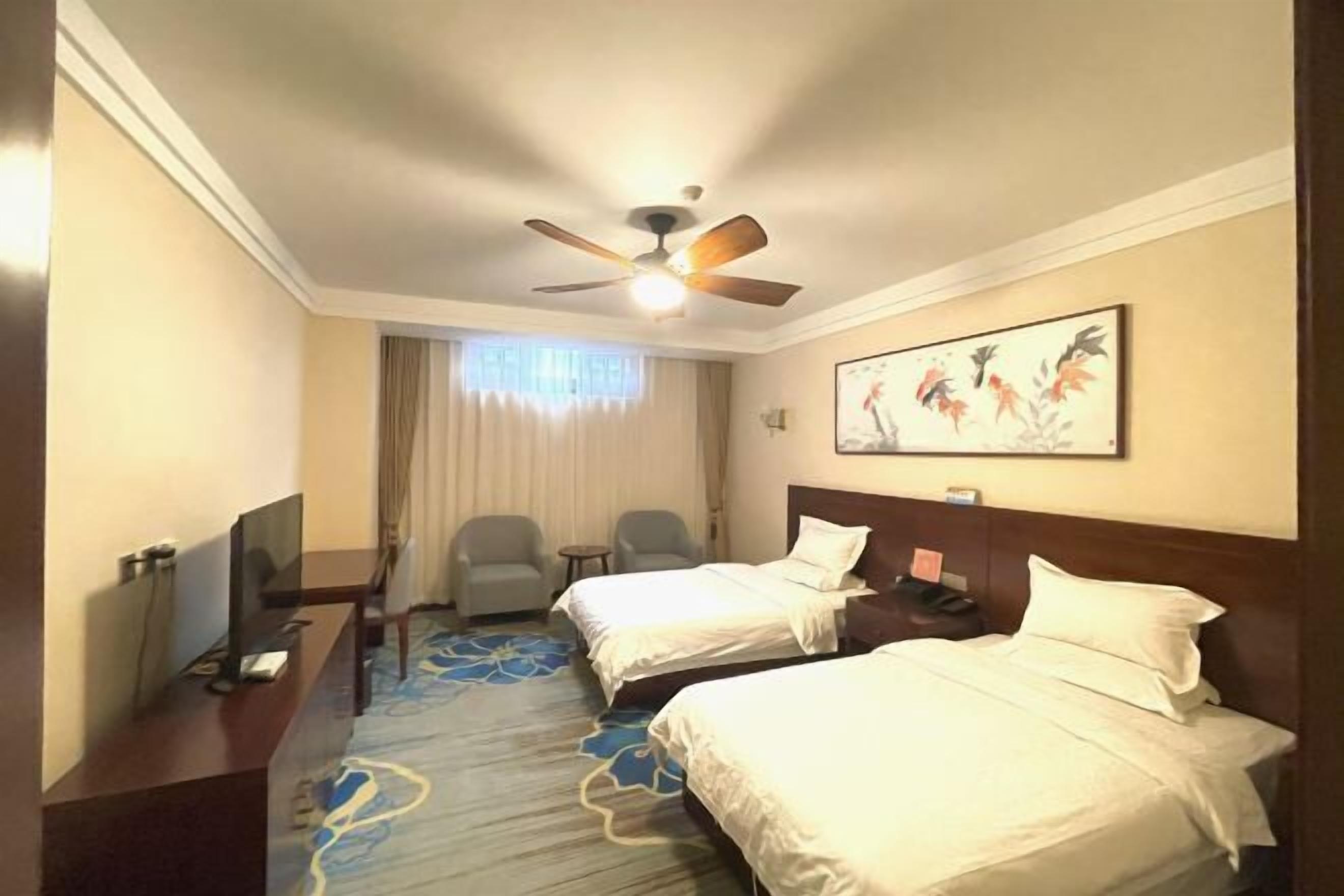 A hotel room with two beds, a ceiling fan, a flat-screen TV, a desk, and a chair.