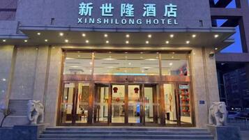 The exterior of the Xinshilong Hotel with a clear entrance, a sign above the doors, and a statue on the left.