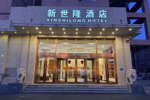 Exterior del Hotel Xinshilong, con entrada despejada, un letrero sobre las puertas y una estatua a la izquierda.