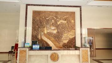A reception desk with a large decorative wall, a clock, and a small plant.