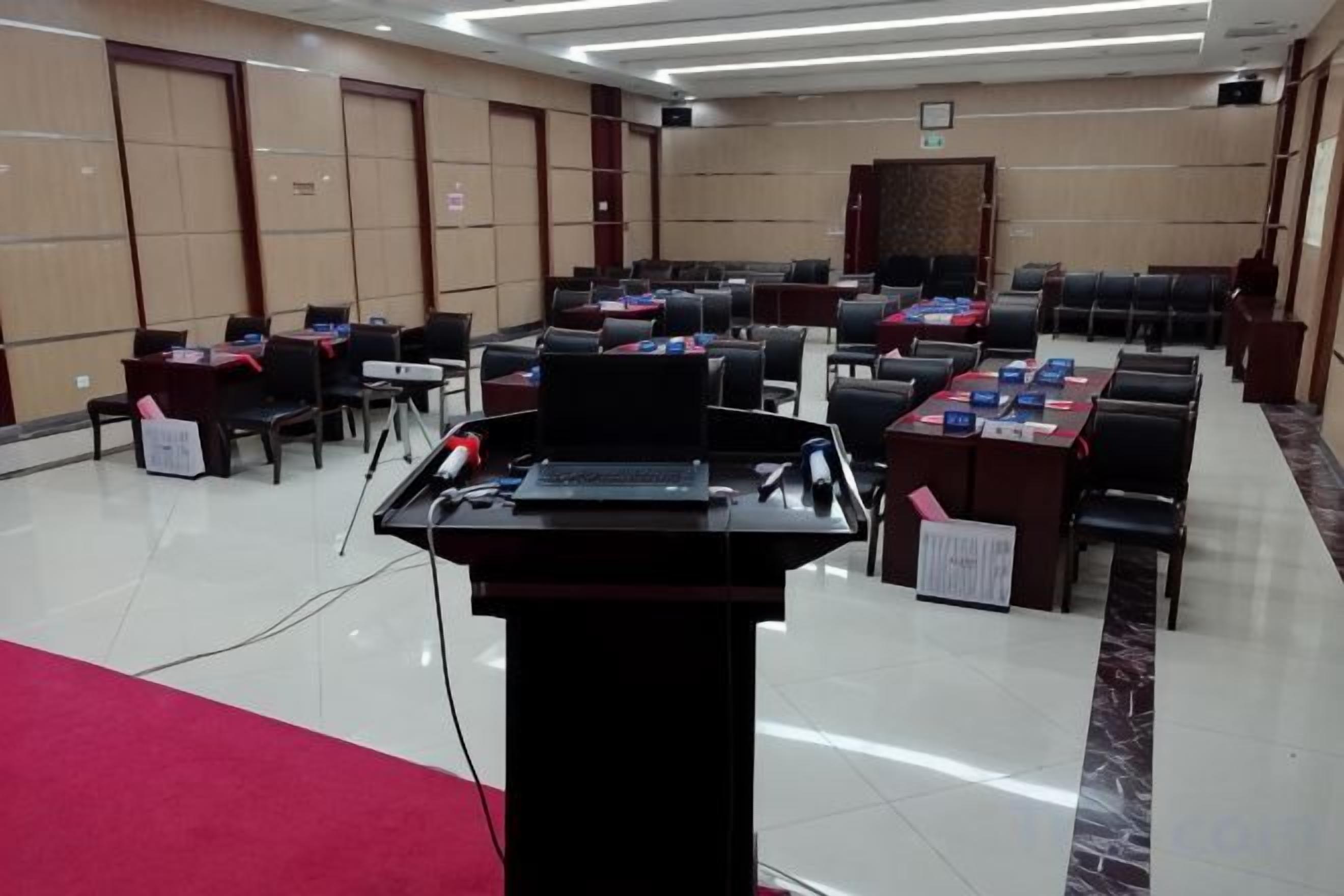 A conference room with multiple tables and chairs, a podium, and a red carpet.