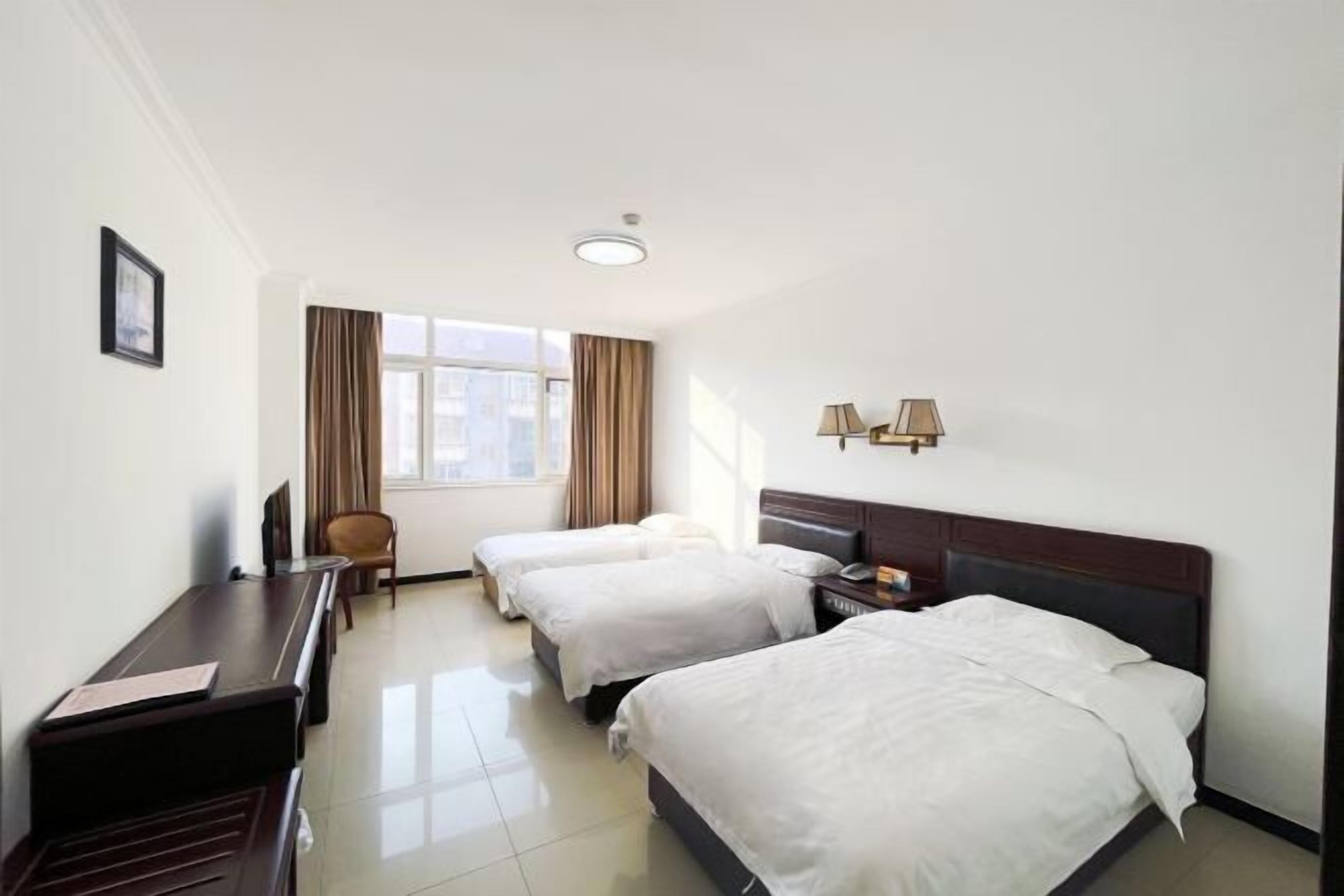 Een hotelkamer met twee bedden, een bureau, een stoel, een raam met gordijnen en een lamp.