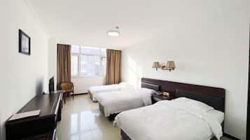 Een hotelkamer met twee bedden, een bureau, een stoel, een raam met gordijnen en een lamp.