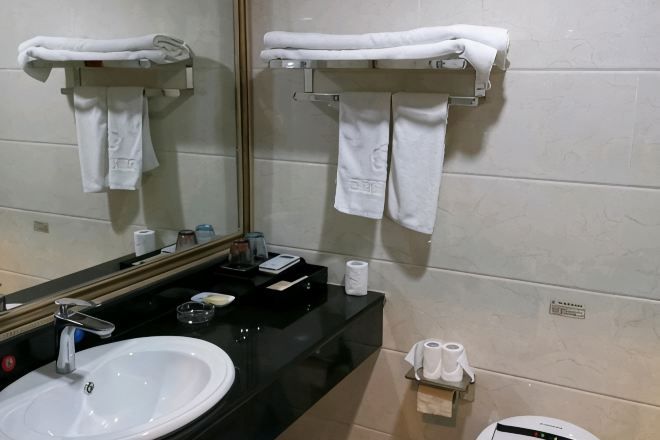 A bathroom with a sink, mirror, towel rack, and toilet paper dispenser.