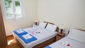 A hotel room with two beds, each with a blue towel and a white towel. There are two bedside tables with lamps, and a window with a view of greenery. - Charming Seaside Escape in Kotor - One Bedroom Apartment with Garden 3 (Donji Stoliv)