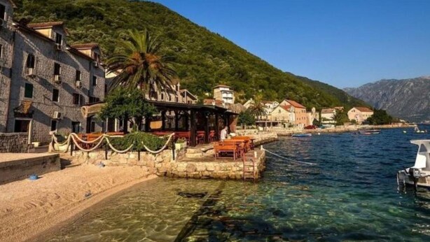 A coastal town with stone buildings, a clear waterfront, and a mountain backdrop.