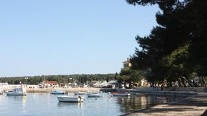 Zona frente al mar con barcos amarrados al muelle, una playa de arena y edificios al fondo.