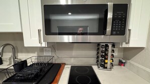 Una cocina con microondas de acero inoxidable, horno empotrado, estufa y escurreplatos.