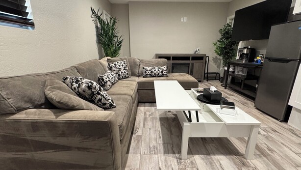 Una sala de estar moderna con un sofá seccional, una mesa de centro blanca y una cocina con refrigerador y microondas.