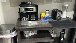 Una kitchenette equipada con cafetera, tostadora, licuadora y un cubo de basura.