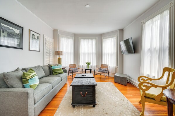 A modern living room with a grey sofa, two armchairs, a coffee table, and a TV mounted on the wall. - Walk to Harvard Square: Apartment in Cambridge (Cambridge)