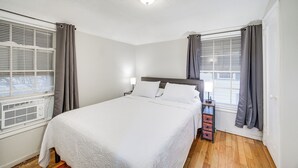 Een netjes ingerichte slaapkamer met een groot bed, een nachtkastje, een lamp en een raam met gordijnen.
